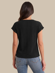 A woman viewed from the back wearing a black short-sleeve ribbed top and light blue jeans against a solid beige background.