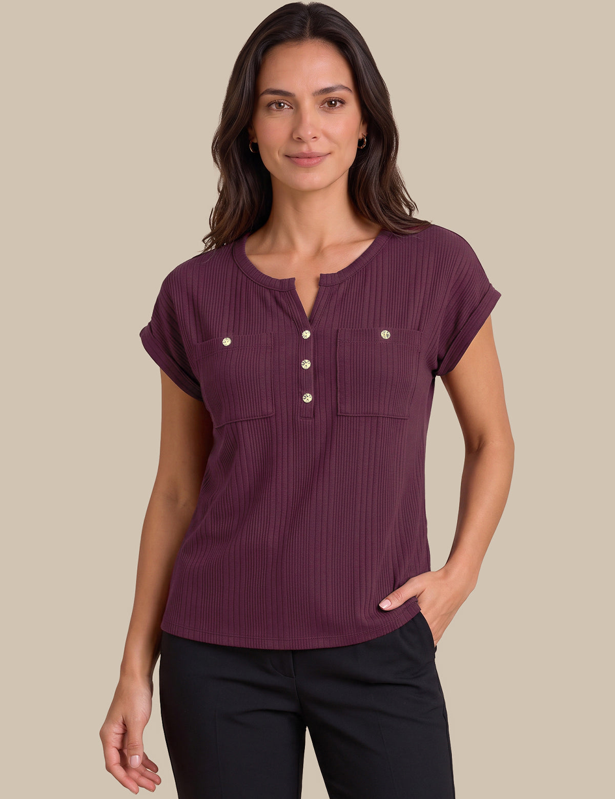 A woman modeling a short-sleeve ribbed henley top in deep plum purple with gold-tone buttons, paired with black pants, against a solid beige background.