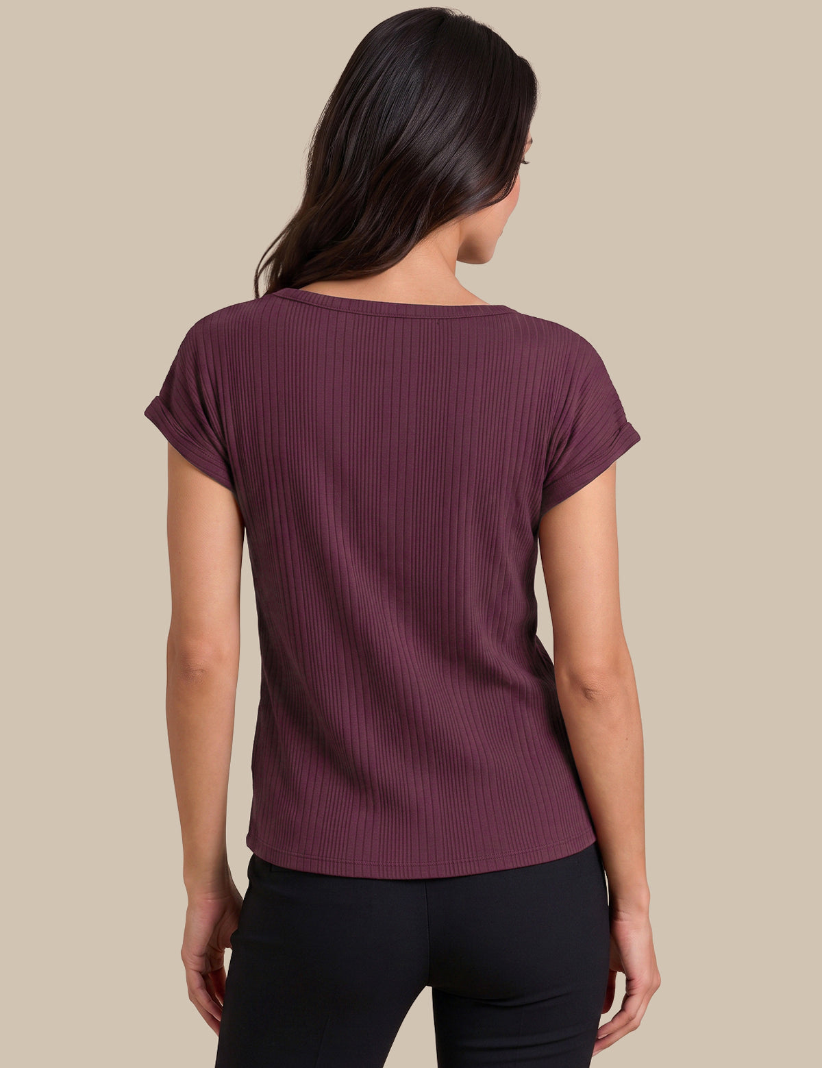 A woman shown from the back wearing a short-sleeve ribbed knit top in a deep plum purple color, paired with black pants, against a solid beige background.