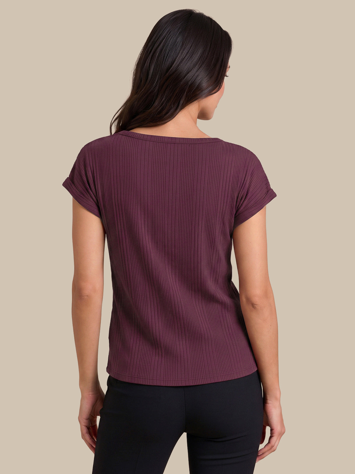 A woman shown from the back wearing a short-sleeve ribbed knit top in a deep plum purple color, paired with black pants, against a solid beige background.