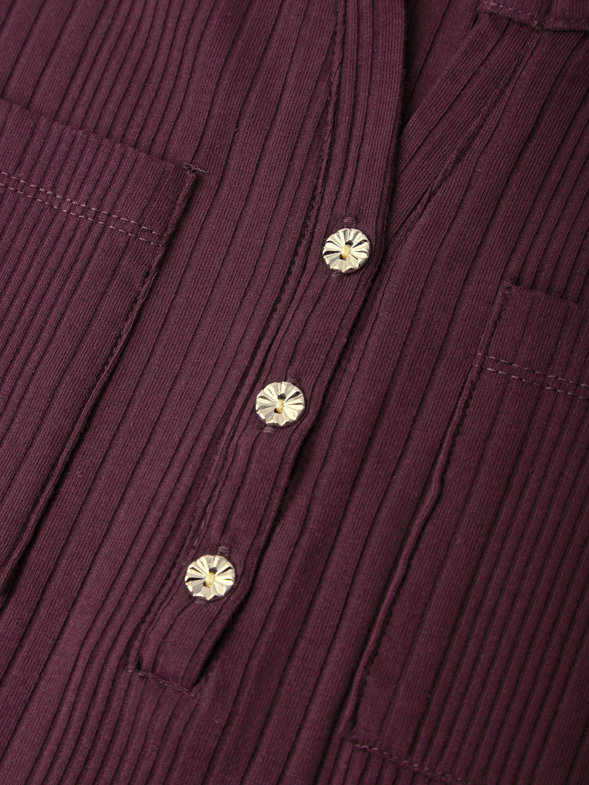 Close-up of a ribbed burgundy corduroy shirt with decorative metallic buttons.