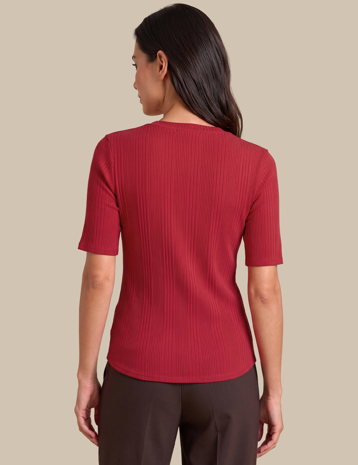 A woman shown from the back wearing a short-sleeve ribbed knit top in a deep red or burgundy shade, paired with dark brown pants, against a solid beige background.