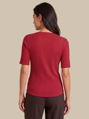 A woman shown from the back wearing a short-sleeve ribbed knit top in a deep red or burgundy shade, paired with dark brown pants, against a solid beige background.