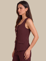 A woman modeling a sleeveless dark burgundy vest with gold-tone buttons down the front, paired with matching pants, against a solid beige background.
