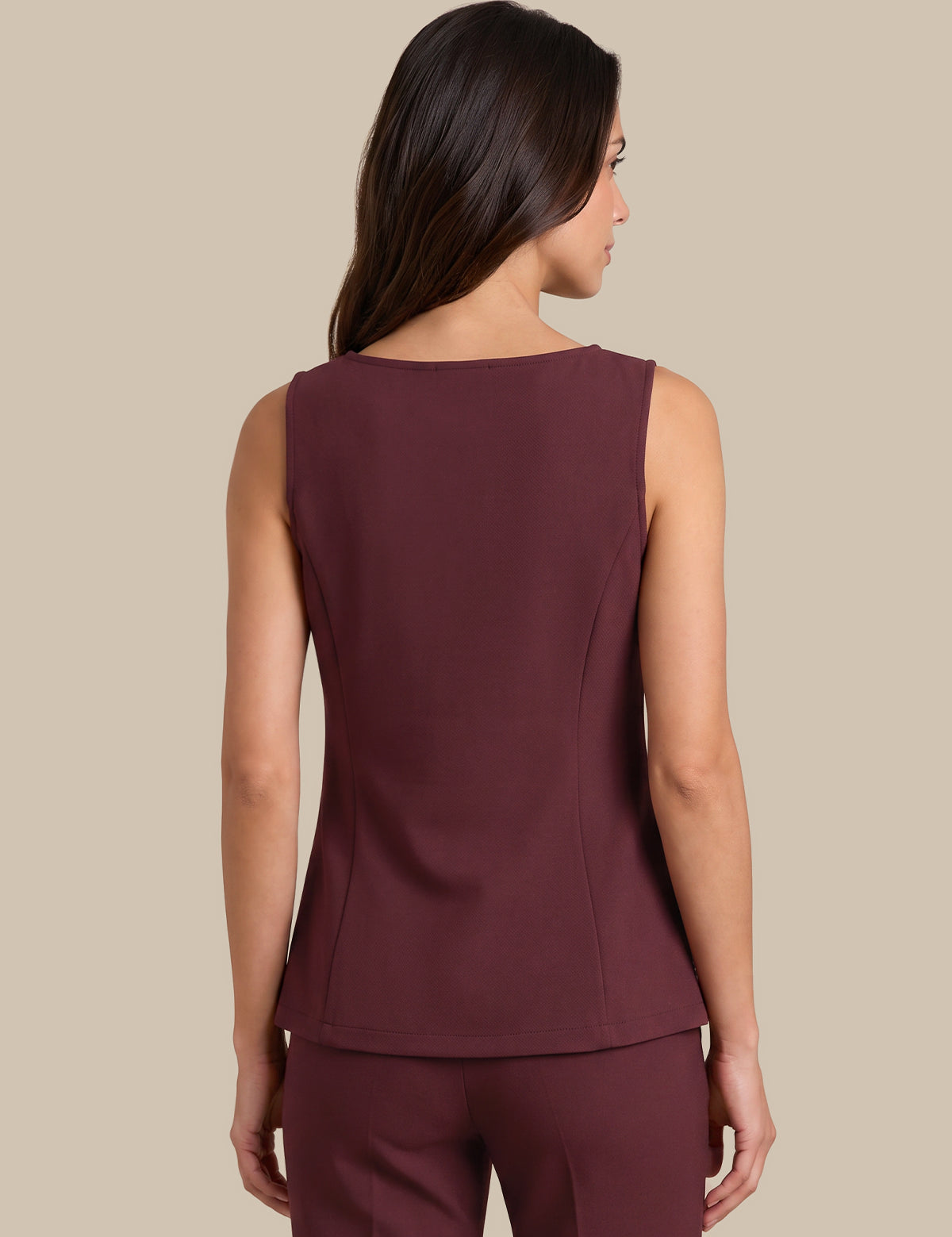 A woman shown from the back wearing a sleeveless, structured peplum-style top and matching pants in a deep burgundy or maroon color, set against a solid beige studio background.