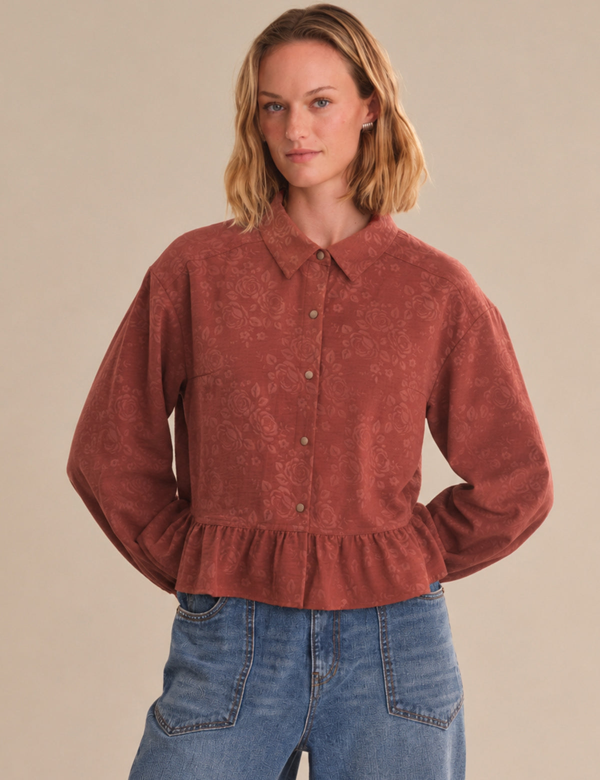 Woman wearing a red corduroy shirt and blue jeans against a beige background