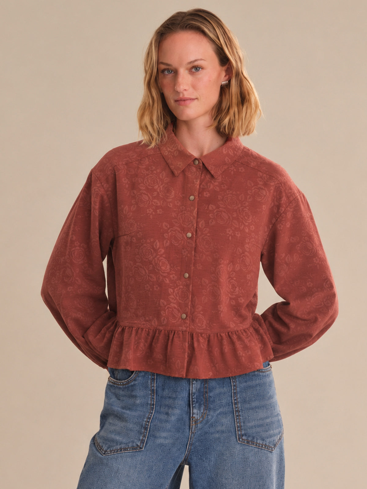 Woman wearing a red corduroy shirt and blue jeans against a beige background