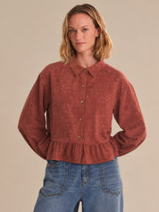 Woman wearing a red corduroy shirt and blue jeans against a beige background