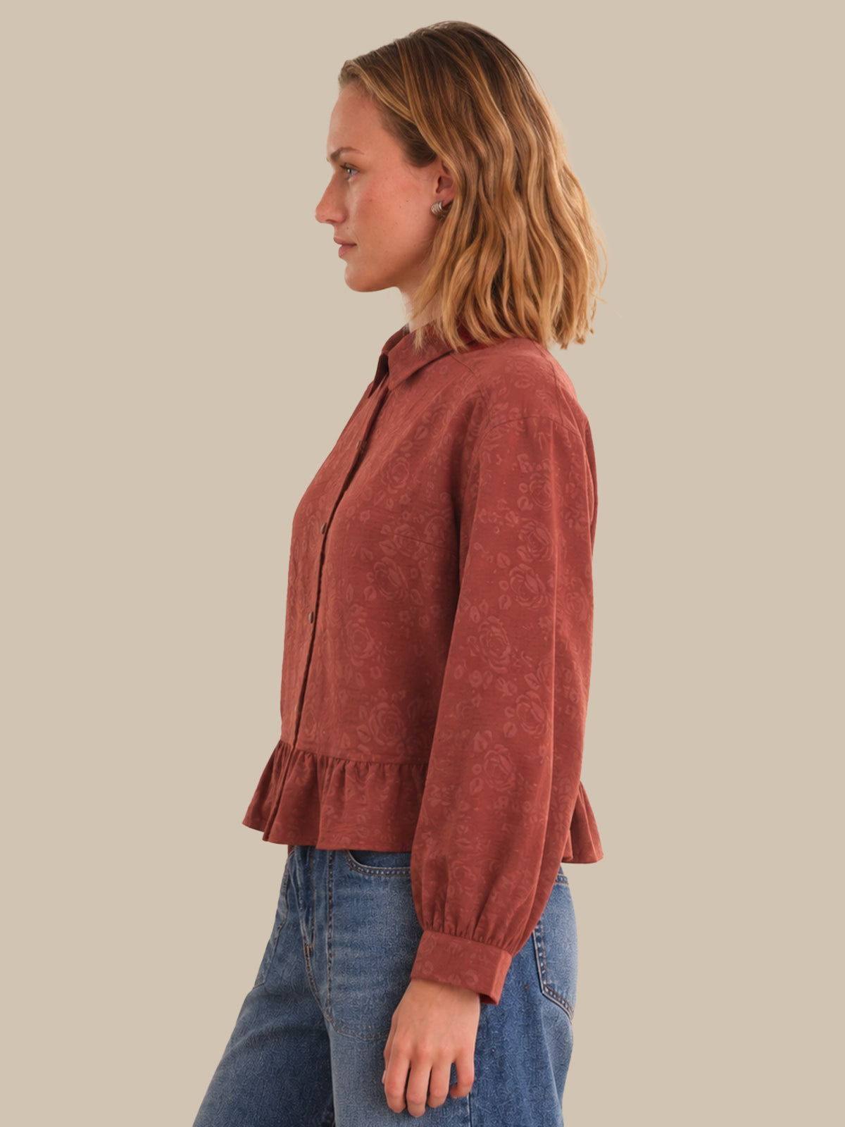 Woman wearing a brown corduroy shirt and blue jeans against a beige background