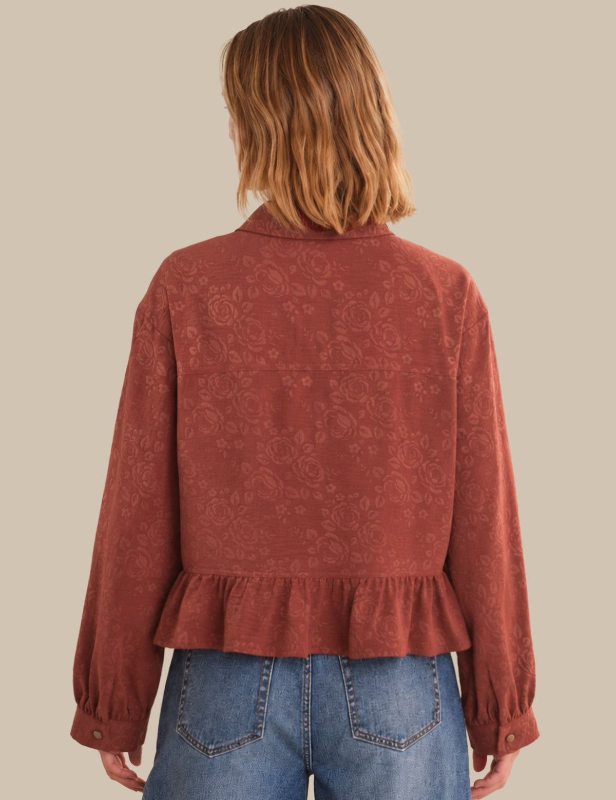 Person wearing a rust-colored patterned blouse with blue jeans on a beige background