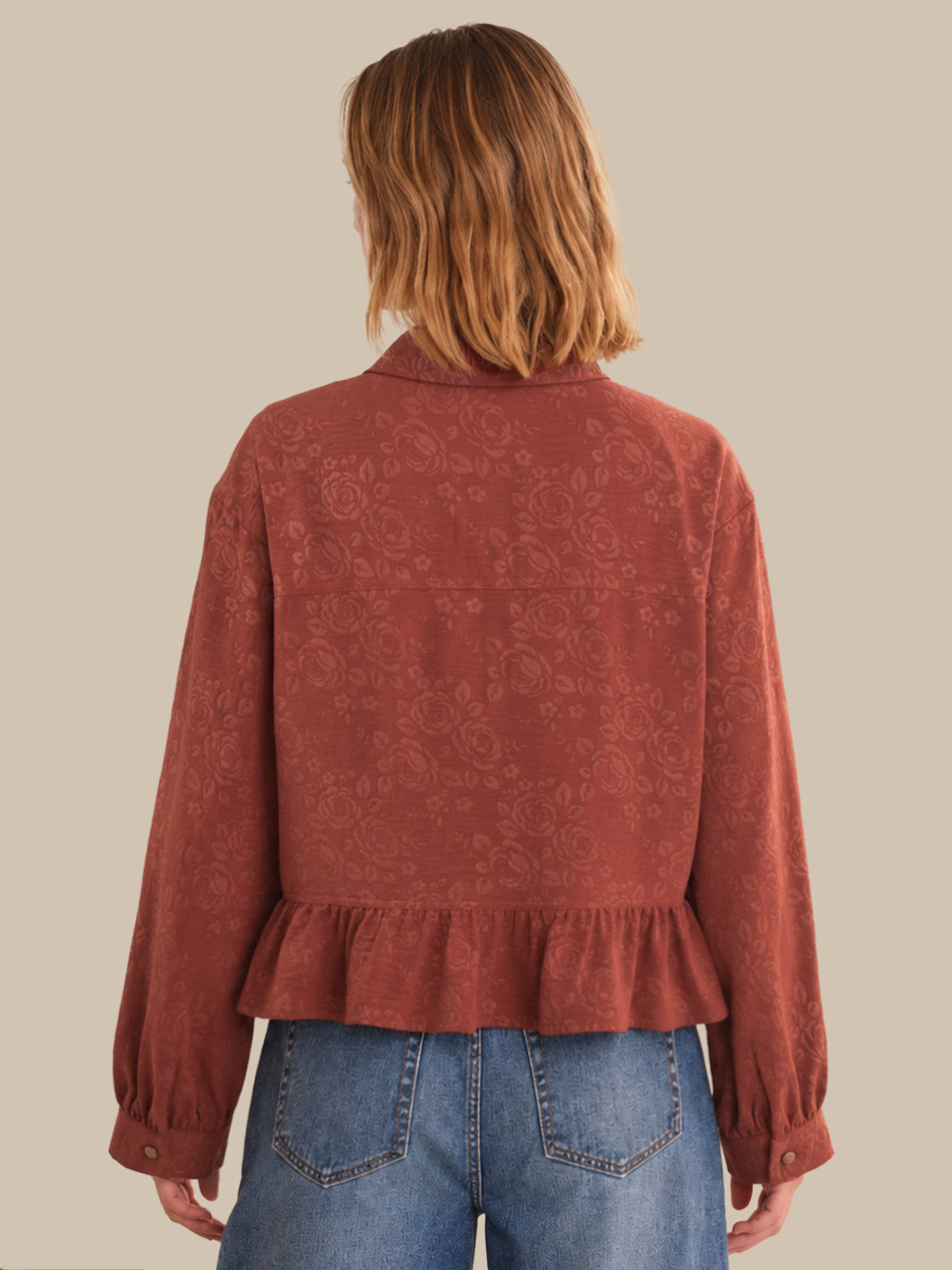 Person wearing a rust-colored patterned blouse with blue jeans on a beige background