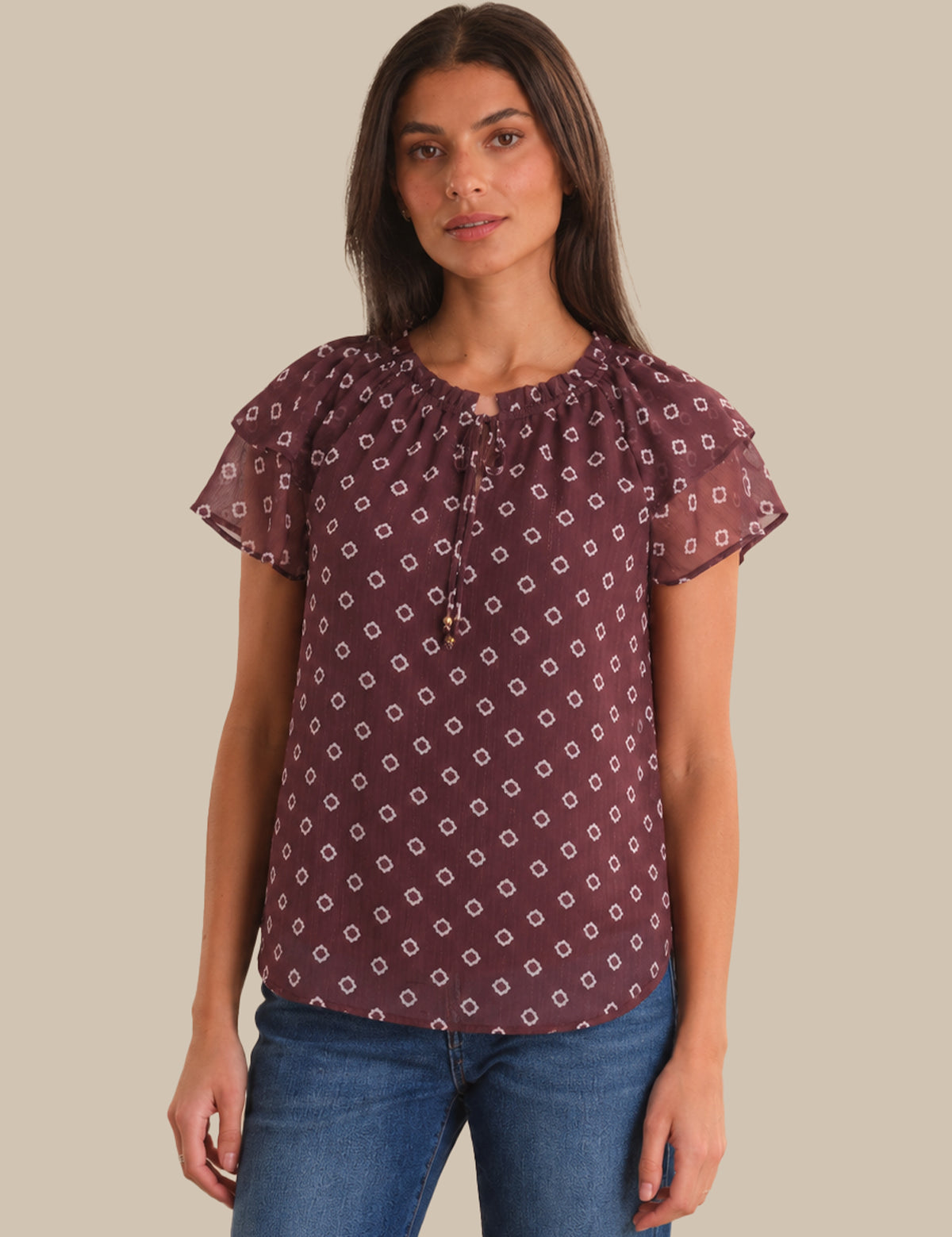 Woman wearing a patterned blouse and jeans on a plain background
