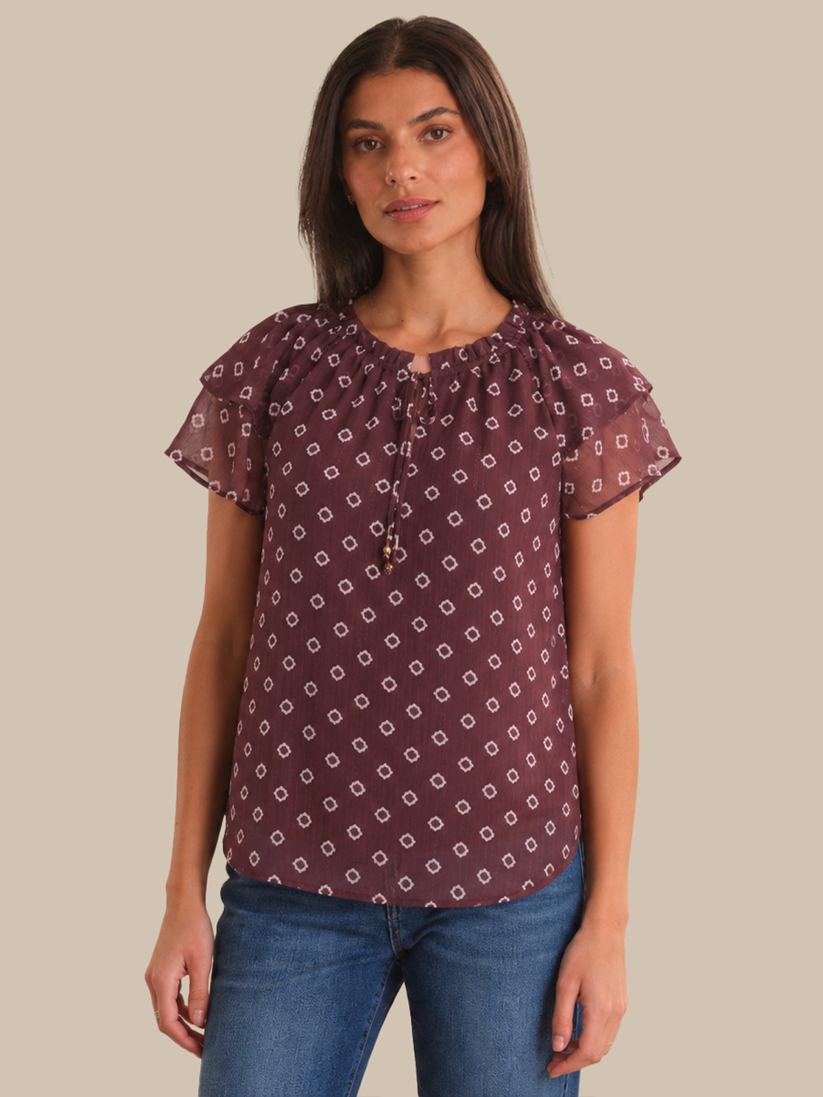 Woman wearing a patterned blouse and jeans on a plain background