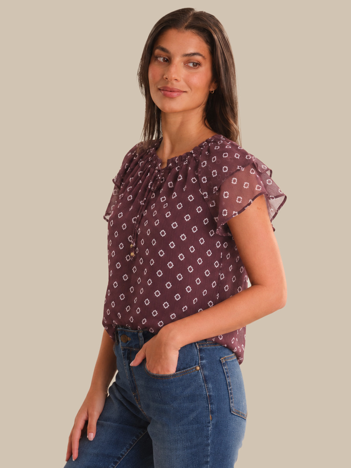 Woman wearing a patterned top and jeans on a beige background