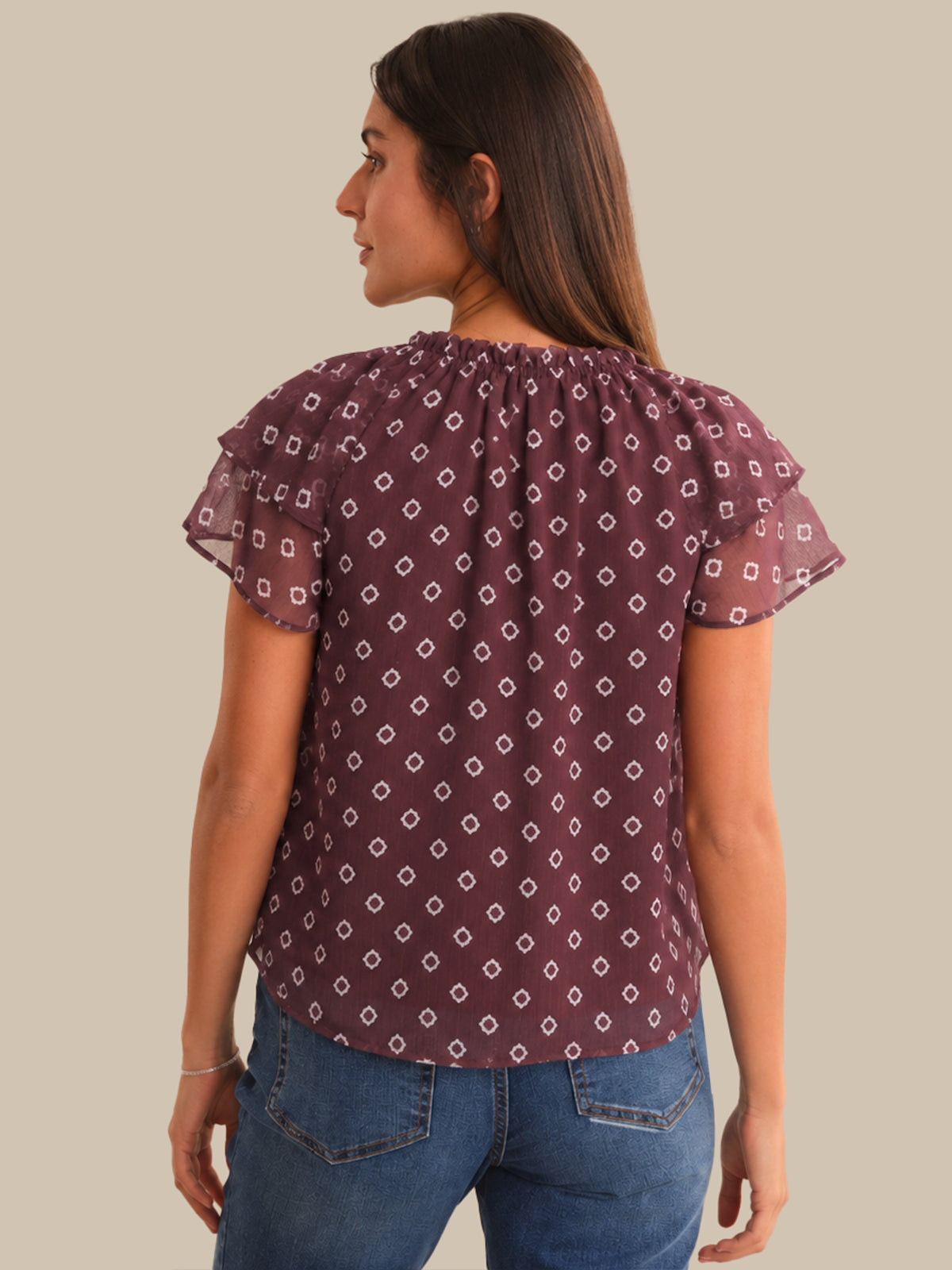 Woman wearing a patterned purple blouse and blue jeans on a beige background