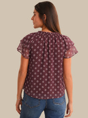 Woman wearing a patterned purple blouse and blue jeans on a beige background