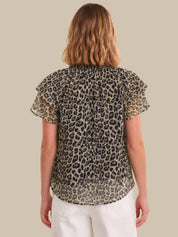 Woman wearing a leopard print blouse with ruffled sleeves on a beige background