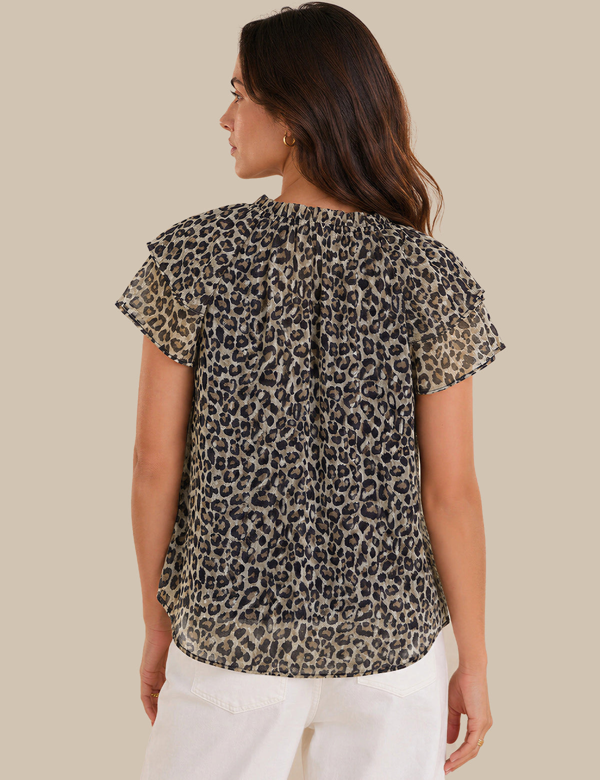 A woman shown from the back wearing a short-sleeve leopard print blouse with a gathered back and white pants, against a solid beige background.