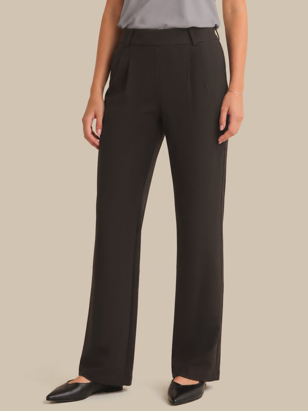 A model wearing dark brown wide-leg trousers with a gray top and black pointed flats, shown from the waist down against a solid beige background.