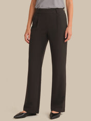 A model wearing dark brown wide-leg trousers with a gray top and black pointed flats, shown from the waist down against a solid beige background.