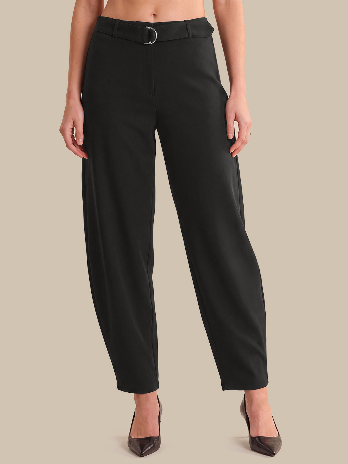 A model wearing black barrel-leg cropped trousers with a matching black belt featuring a silver-toned ring, paired with dark brown pointed-toe heels, set against a solid beige background.