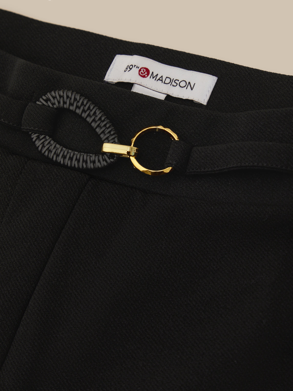 Black pants with a gold belt buckle and 'Madison' label on a beige background