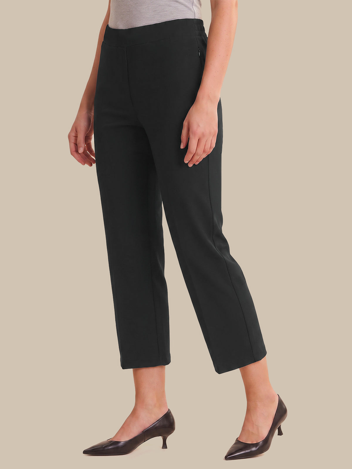 A model wearing black cropped ankle-length trousers with a wide-leg fit, paired with dark brown pointed-toe kitten heels and a light gray top, set against a solid beige background.
