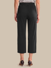 A model shown from the back wearing black cropped pants with a wide elastic waistband, paired with dark brown pointed-toe heels against a solid beige background.