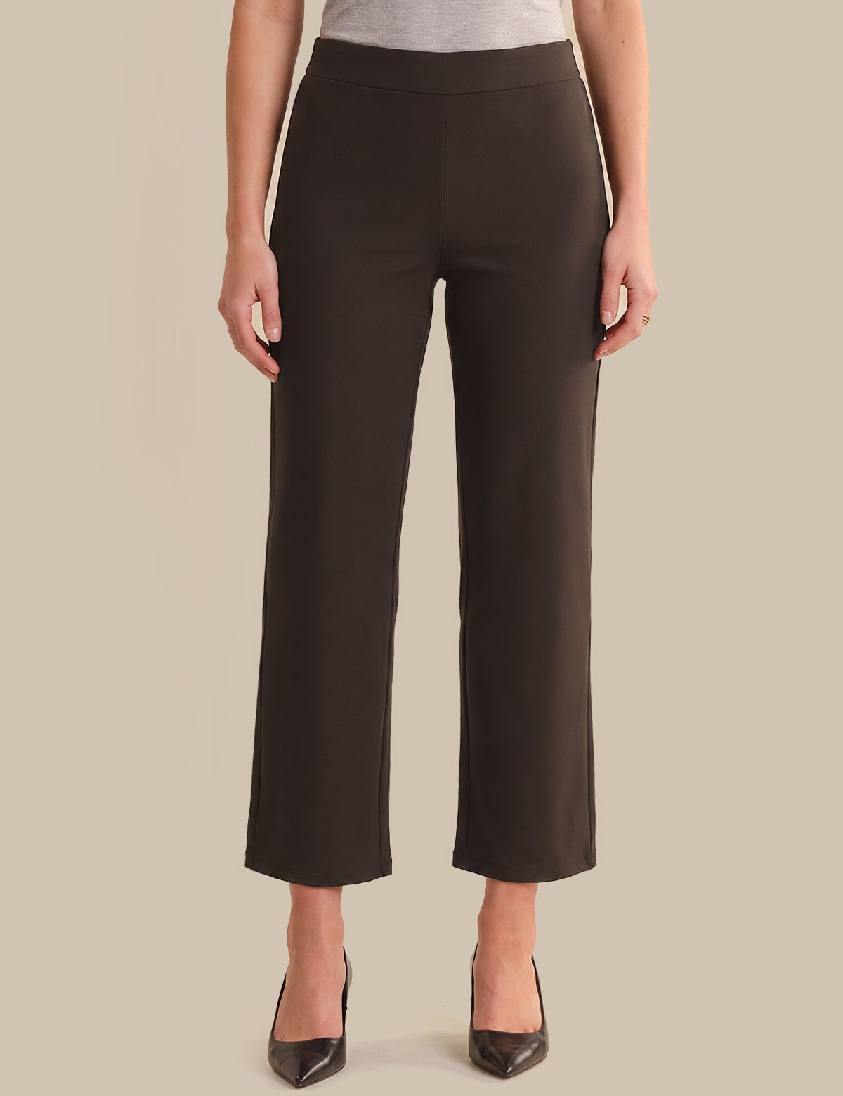 A model wearing dark brown cropped wide-leg trousers with a gray top and black pointed-toe heels, shown from the waist down against a solid beige background.