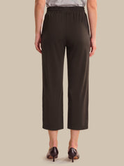 A model shown from the back wearing dark brown cropped trousers, a light gray top, and dark brown pointed-toe heels against a solid beige background.