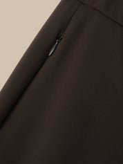 Close-up of a dark brown fabric garment showing a diagonal seam and a small black zipper pull on a light beige background.