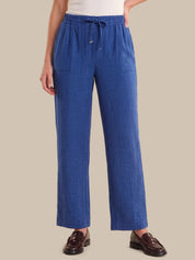 A person wearing blue wide-leg drawstring pants with a textured linen-like fabric, paired with a white top and brown leather loafers, against a solid beige background.