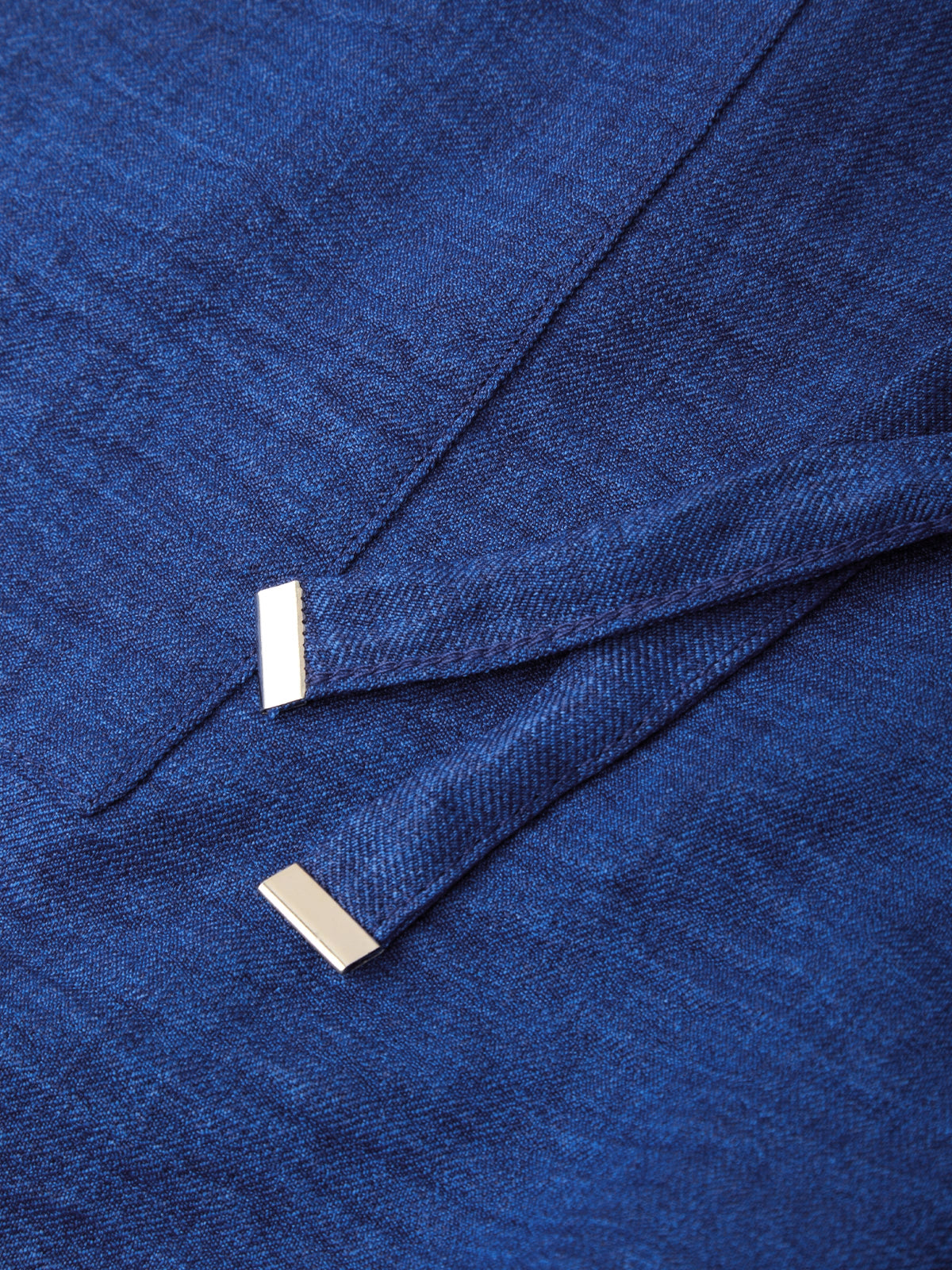 A close-up of a textured royal blue fabric, likely a wool or cashmere sweater, featuring two small, polished silver rectangular bar pins attached near the fold.