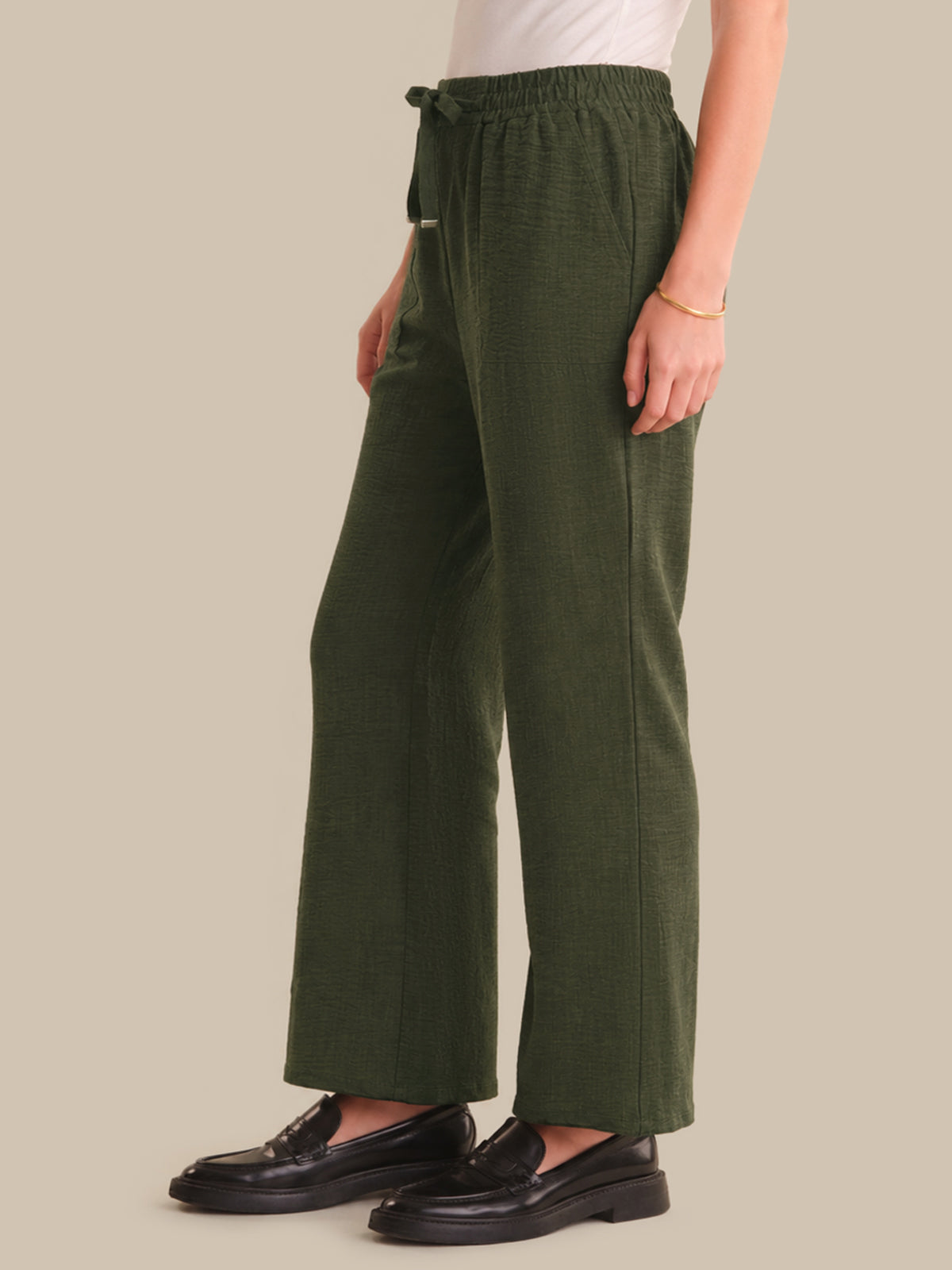 Person wearing green pants and black shoes on a plain background