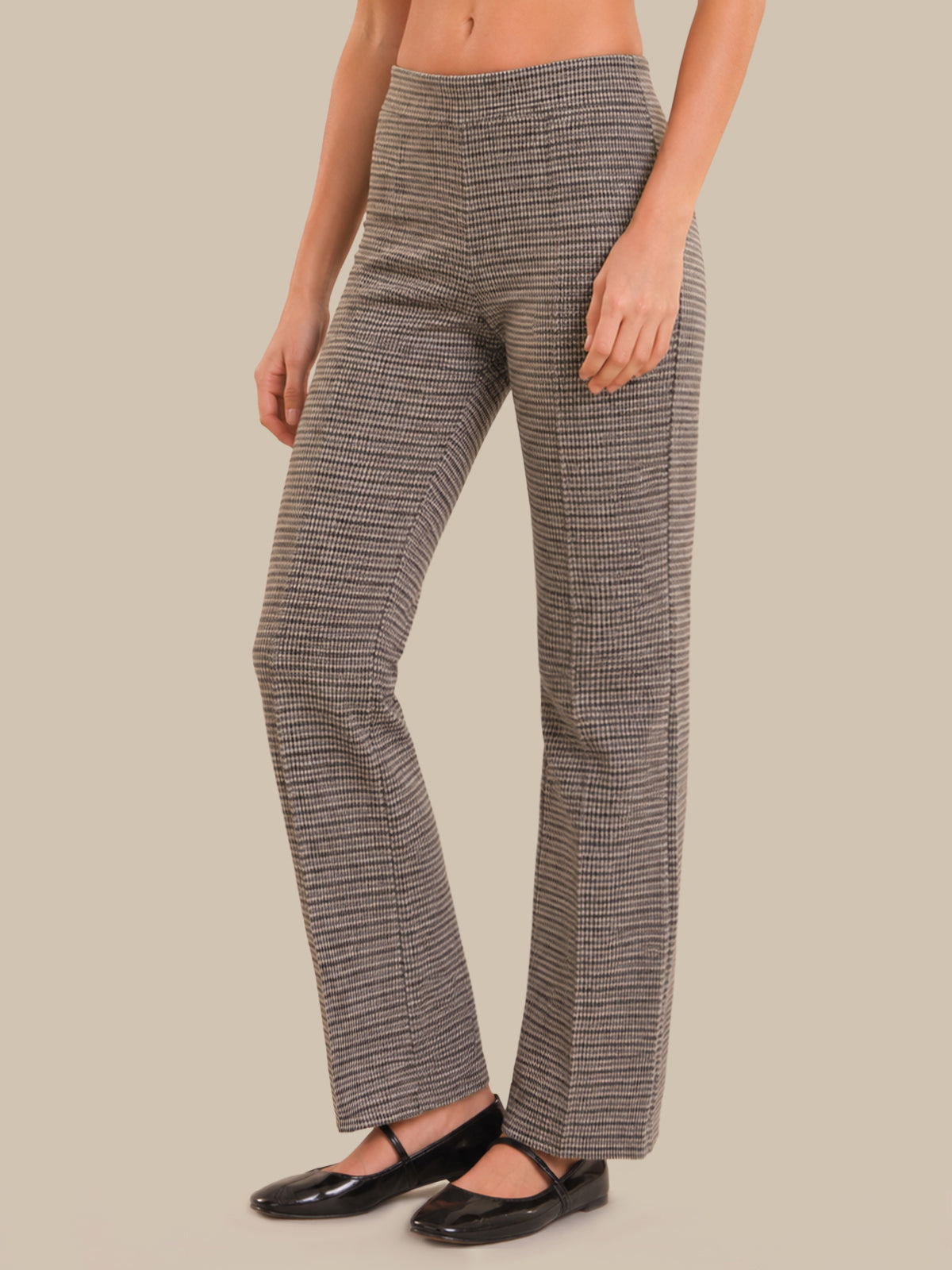A model wearing high-waisted, straight-leg trousers with a fine black and white micro-pattern, paired with black flat shoes, against a solid beige background.