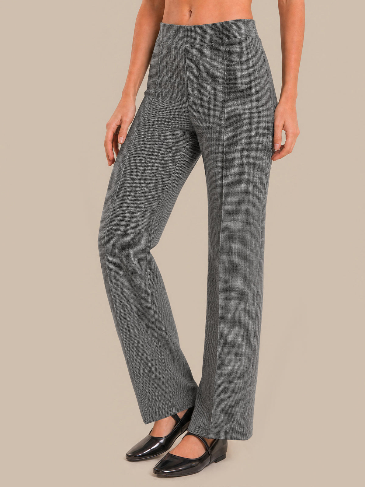 A model wearing high-waisted, wide-leg gray trousers with a subtle textured pattern, paired with black flat shoes, against a solid beige background.