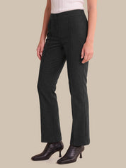 A model wearing dark charcoal gray straight-leg trousers, paired with a white ribbed top and dark brown leather ankle boots, set against a solid beige background.