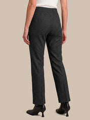A model shown from the back wearing dark charcoal gray straight-leg trousers, a white ribbed top, and black ankle boots against a solid beige background.