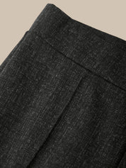 Close-up of dark charcoal gray textured fabric, showing a fine woven pattern and a folded waistband detail, set against a solid beige background.