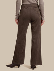 A person shown from the back wearing dark brown wide-leg trousers, a taupe long-sleeve top, and dark heeled boots against a plain beige studio background.