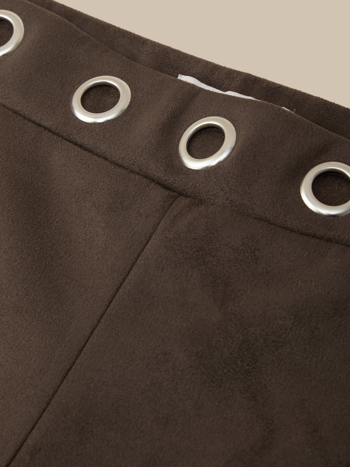 Close-up of dark brown suede-like fabric with a waistband and four silver metal grommets, set against a light beige background.