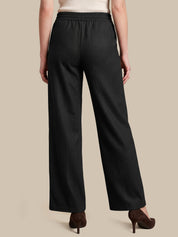 A person shown from the back wearing black wide-leg pants with an elastic waistband, paired with a light top and brown heels, against a plain beige studio background.