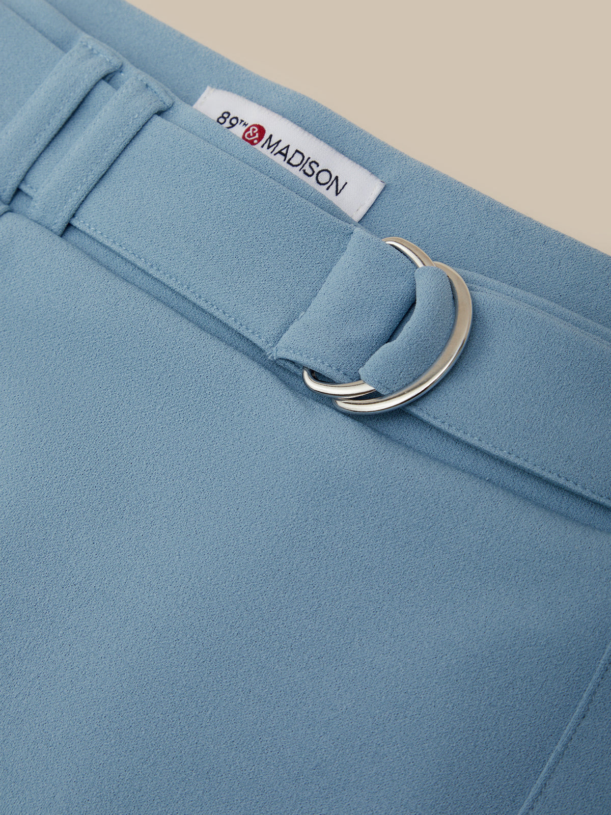 Close-up of a light blue garment with a belt and '89 Madison' label.