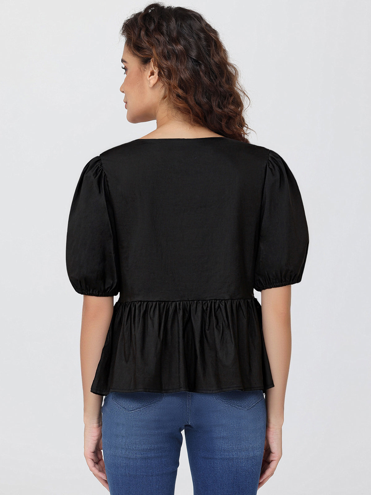 Woman wearing a black blouse with puffed sleeves and a ruffled bottom on a white background