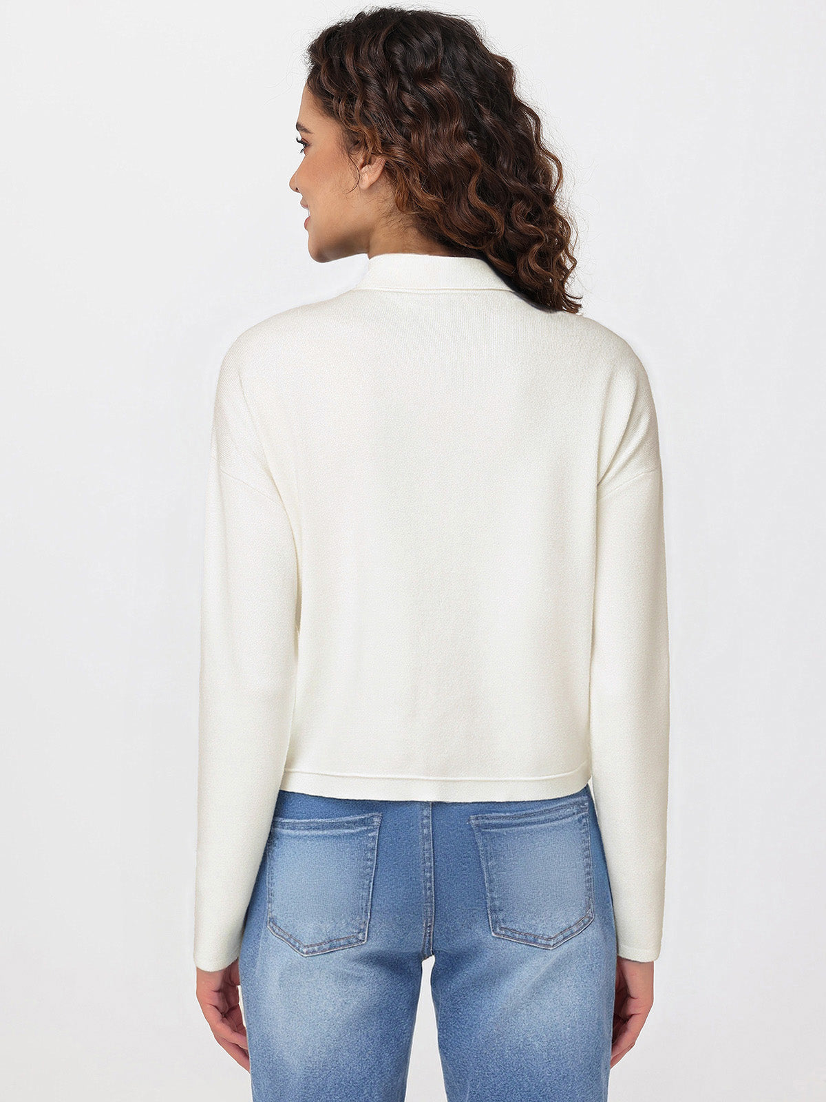 Woman wearing a white long-sleeve cardigan and blue jeans on a light gray background