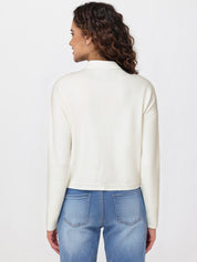 Woman wearing a white long-sleeve cardigan and blue jeans on a light gray background