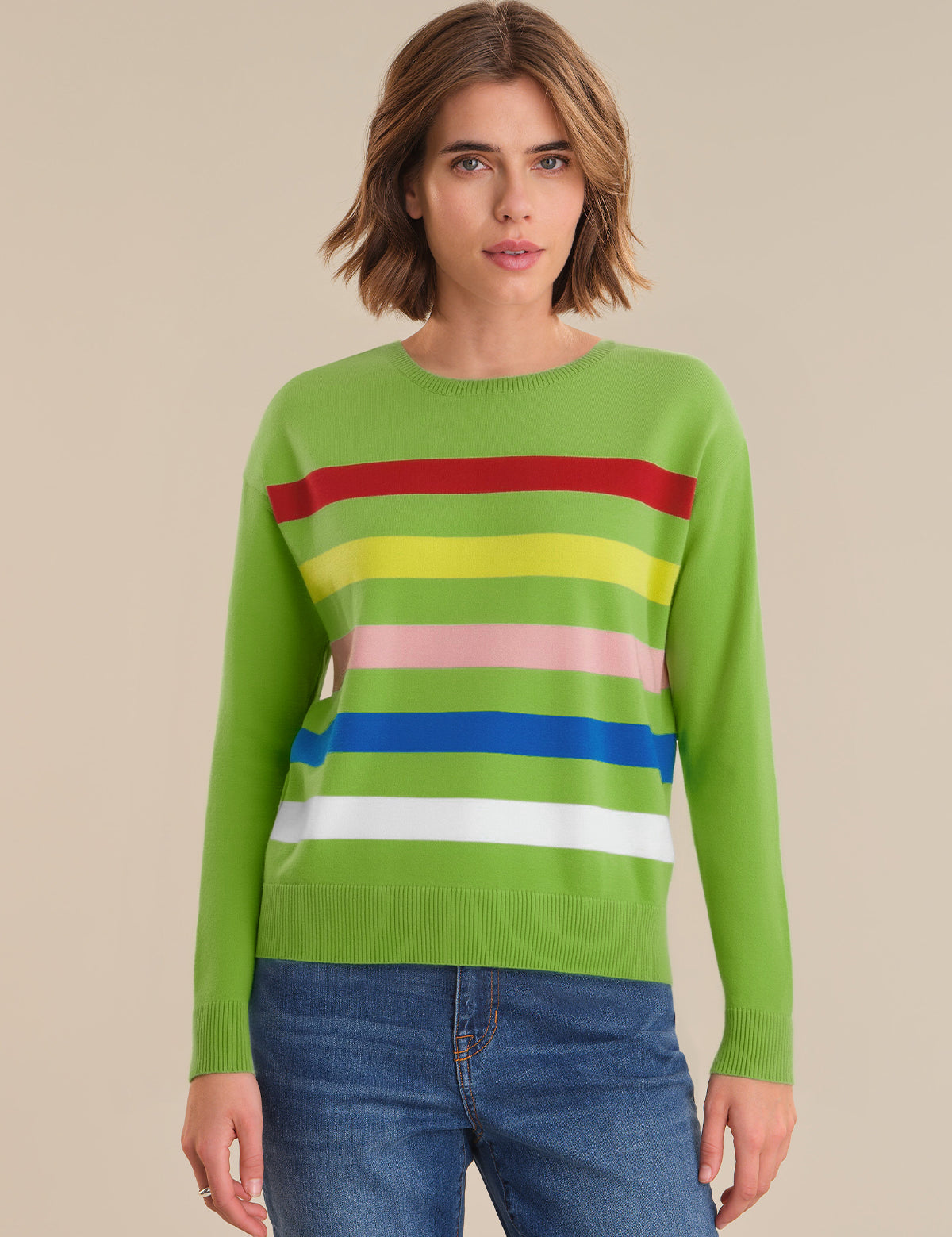Woman wearing a green sweater with colorful stripes on a beige background