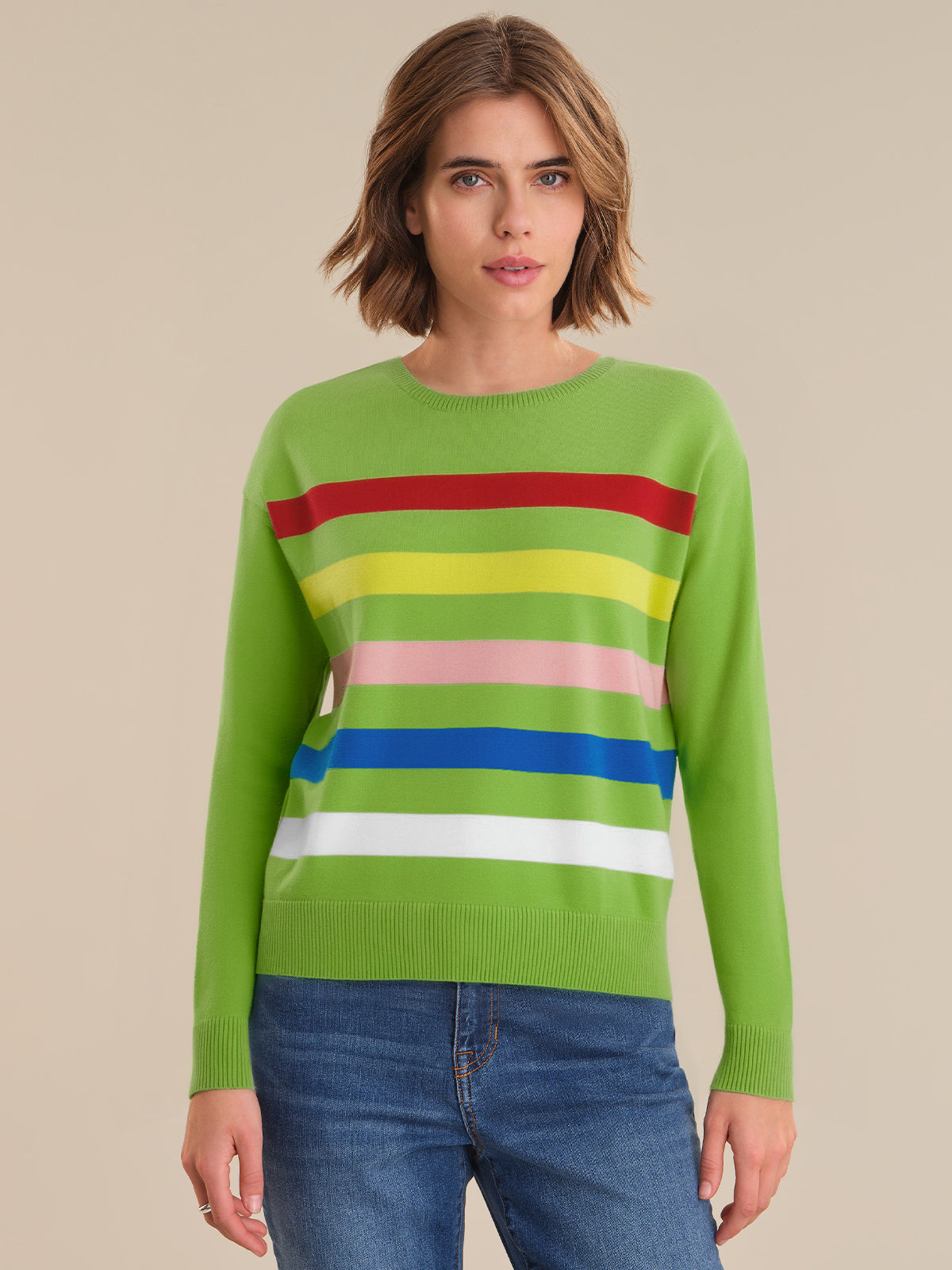 Woman wearing a green sweater with colorful stripes on a beige background