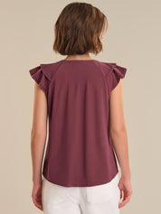 Person wearing a burgundy top with ruffled shoulders on a beige background