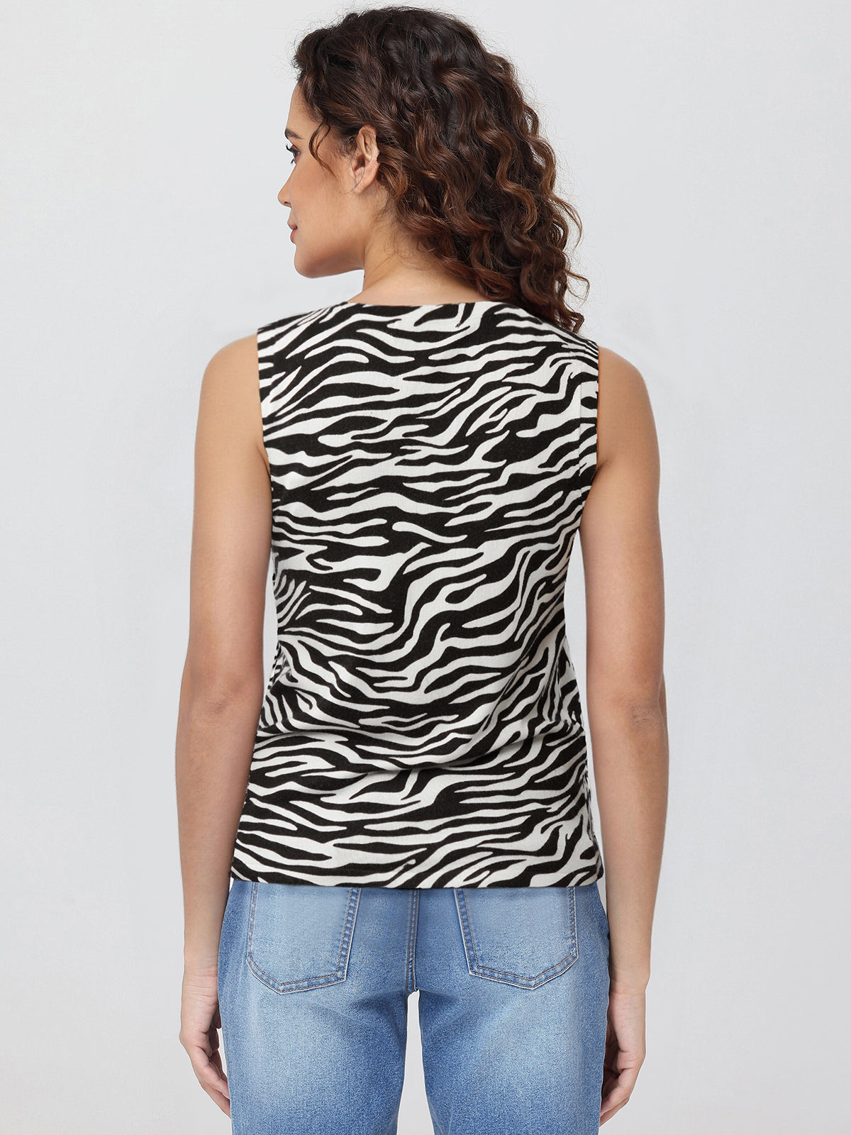 Woman wearing a zebra print sleeveless top and blue jeans on a white background